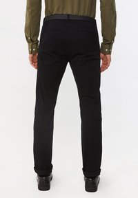 Black trousers made of soft fabric, featuring a slim-fit design, belt loops, and two back pockets. Rolled cuffs above ankle-length.