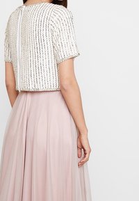 Perlbroderad kort topp i elfenben med korta ärmar; har en dragkedja bak. Matchad med en svävande ljusrosa tulekjol.