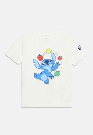 T-shirt blanc à manches courtes avec un personnage de dessin animé bleu jonglant avec un citron, une fraise, une pomme et une tomate à l'avant.