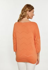 Lekki pomarańczowy sweter dzianinowy z wzorem w zygzak stworzonym przez otwarte dziurki, z rękawami o długości 3/4 i luźnym krojem.