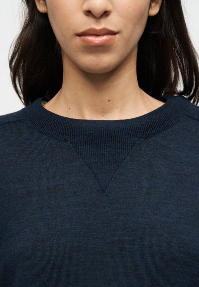 Πλεκτό πουλόβερ σε ναυτικό μπλε χρώμα με ριμπ πλεγμένη λαιμόκοψη και V-σχήμα λεπτομέρεια στο στήθος. Ομαλή υφή με διακριτικές διακυμάνσεις στο χρώμα.