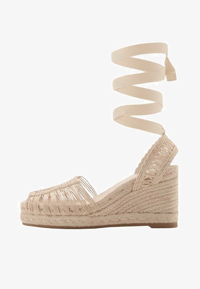 Sandalo con zeppa in espadrille beige, con tomaia in juta intrecciata, punta aperta e una fascia alla caviglia con motivo. Presenta un design con bordo texturizzato e rialzato.
