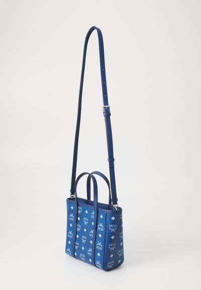 Sac fourre-tout bleu en tissu, présentant un motif logo intégral, deux courtes poignées et une bandoulière longue réglable pour un port en travers.