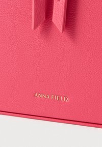 Roosa tekstuuriga kunstnahast käekott, mille alumises osas kuldne logo "ANNA FIELD"; varustatud kahe vertikaalse, lameda rihmaga.