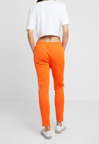 Orange träningsbyxor med slim fit, försedda med vita sidostripes och ett elastiskt midjeband, kombinerat med en vit cropped topp och vita sneakers.