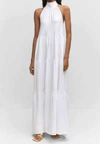 Biała, bezrękawna sukienka maxi z wysokim dekoltem halter, marszczonym bodicem i falbaniastego kroju spódnicy. Wykonana z lekkiego materiału.