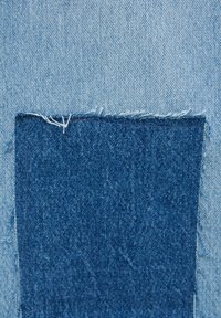 Tissu en denim à lavage bleu clair avec une pièce de tissu bleu plus foncé. La pièce présente des bords effilochés et un tissage texturé.