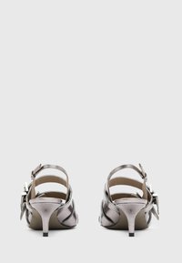 Silver metallic heeled sandals with an open back, featuring strap detailing and a small bow accent. The heel is approximately 5 cm.