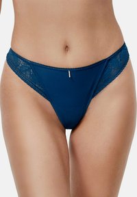 Bikini en dentelle bleu foncé avec un devant en tissu lisse et un petit accent en métal au centre. Il présente une taille modérée et une couverture minimale.