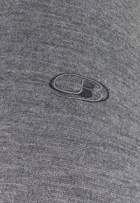 Grau bezogenes Material mit einer glatten Textur. Enthält ein besticktes schwarzes Logo in ovaler Form, zentriert nahe der oberen rechten Ecke des Bildes.