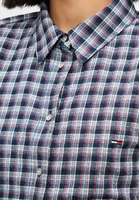 Καρό πουκάμισο με μπλε, λευκά και κόκκινα καρό σχέδια. Σχεδιασμός με κουμπιά και δομημένο γιακά με μικρό λογότυπο στο στήθος.