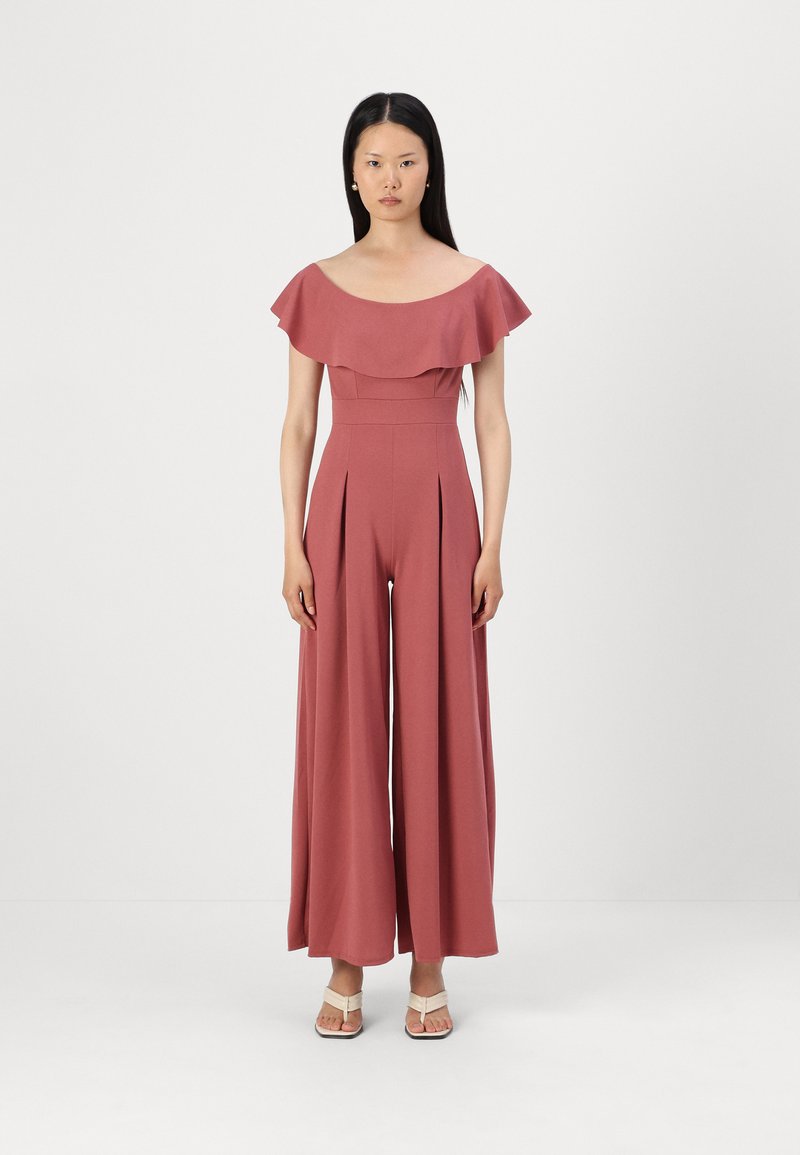 Jumpsuit v malinové barvě s volnými rameny a volánem, úzkým trupem a širokými nohavicemi, vyrobený z hladkého materiálu s vertikálními záhyby.