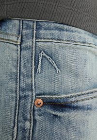 Vaqueros de mezclilla azul claro con un logotipo bordado distintivo en el bolsillo trasero y un remache de cobre de acento en la cinturilla.