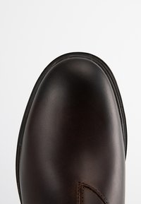 Scarpa in pelle marrone con punta arrotondata e dettagli di cucitura sottili. Presenta un design elegante e minimale con una suola in gomma nera.