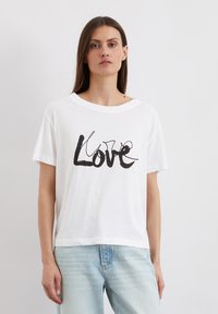 Weiße Baumwoll-T-Shirt mit lockerer Passform, versehen mit einem schwarzen Grafikdruck des Wortes "Love" in geschwungener Schrift. Kurze Ärmel, Rundhalsausschnitt.