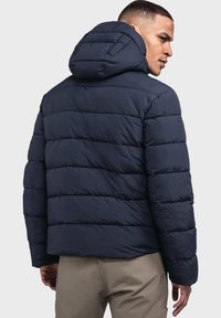 Marineblaue Steppjacke mit horizontalem Steppmuster, verstellbarer Kapuze und elastischen Bündchen, aus leichtem, wasserabweisendem Material.
