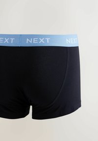 Boxer noir avec une ceinture élastique bleu clair portant le mot « NEXT » en blanc. Le tissu semble lisse et extensible.