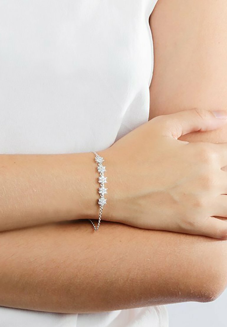 Bracciale argento con molte pietre chiare simili a diamanti disposte a forma di fiori; catene sottili e una texture liscia.