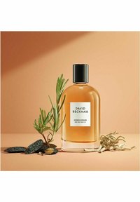 Amber Breeze Eau de Parfum in a clear glass bottle with a black cap, surrounded by green rosemary and dark textured stones on a peach background.