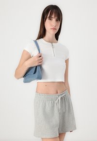 Hvit ribbet crop topp med glidelås foran, kombinert med lysegrå shorts med elastisk midje, og en blå denim skulderveske.