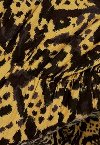 Tkanina w panterkę w odcieniach żółci i brązu, charakteryzująca się miękką fakturą i marszczonymi detalami, prezentująca odważne, nieregularne plamy i wzory.