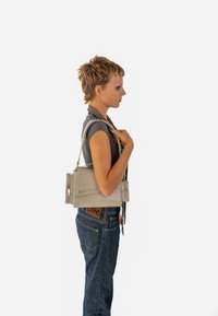 Grau ledere Tasche mit silbernem Zubehör, rechteckiger Form, mit oberem Reißverschluss und dem Logo "EXPATRIÉ" auf der Vorderseite. Am Schulter getragen.