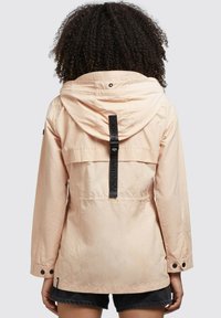 Light pink hooded jacket with a drawstring, featuring a logo strap at the back, buttoned cuffs, and a front pocket at the waist.