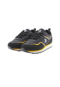 Scarpe sportive nere con tomaia sintetica, dettagli gialli e suola bianca. Presentano lacci rotondi e una suola in gomma con texture.