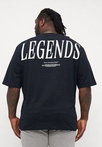Navy blue short-sleeve t-shirt featuring large white "LEGENDS" text on the back and smaller text below. Soft fabric with a relaxed fit.