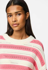 Pull rayé avec des teintes roses et blanches, motif tricoté, encolure côtelée et manches courtes. Tissu léger et texturé.