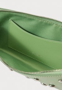 Zaļš maciņš ar rāvējslēdzēju, gludu ārpusi, metāla akcentiem un iekšējo karšu kabatu. Oderēts ar mīkstu audumu izturībai.