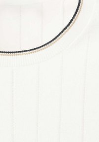 Gros plan sur un tissu tricoté blanc côtelé avec un col rond bordé d'une couture décorative noire et beige.