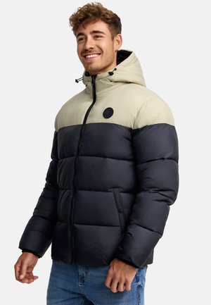 Chaqueta acolchada con capucha, con la mitad superior en color beige y la mitad inferior en color navy, que presenta un parche con el logotipo en negro, cremallera y bolsillos laterales.