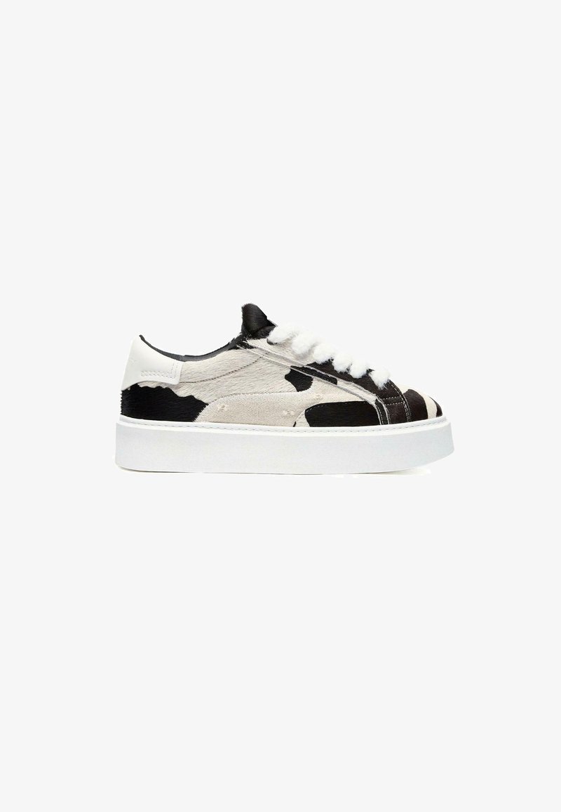 Baltie sneakers ar melnu un pelēku govs rakstu, teksturētu virsu, auklu aizdari un biezu baltu platformas zoli.