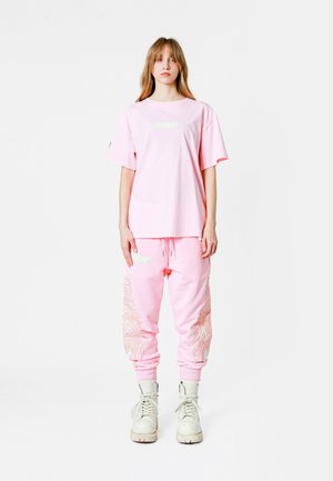 Camiseta oversized rosa y joggers a juego con acentos bordados. El conjunto presenta un diseño relajado y una tela suave, combinado con botas blancas.
