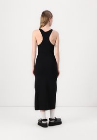 Abito nero, aderente, senza maniche con scollatura a barca; lunghezza al ginocchio. Il modello indossa scarpe nere chunky con suola platform e calzini bianchi.
