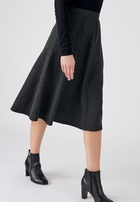 Zwarte A-lijn rok met een gestructureerd geometrisch patroon, middellang, gecombineerd met zwarte enkelboots met een zijrits en blokhak.