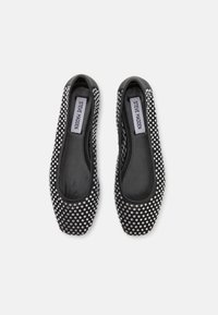Pantofi negri plat, cu o textură netedă, decorați cu strasuri argintii pe partea superioară. Eticheta spune "Steve Madden".