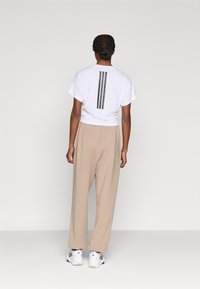 Λευκό κοντό μπλουζάκι με γκρι ρίγες στην πλάτη, συνδυασμένο με μπεζ παντελόνι σε φαρδιά γραμμή και λευκά αθλητικά παπούτσια. Ομαλό ύφασμα και χαλαρή σχεδίαση.