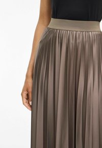 Jupe plissée taille haute en ton taupe métallisé, fabriquée dans un tissu lisse avec un léger éclat ; dotée d'une large ceinture élastique.