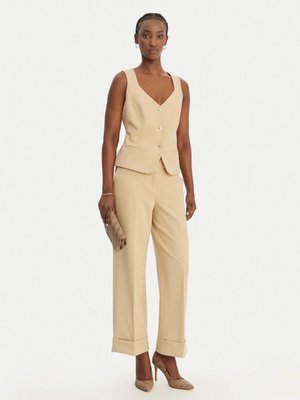 Femme portant un gilet beige sans manches boutonné et un pantalon large assorti, tenant une pochette à motifs et portant des talons hauts en peau de serpent.