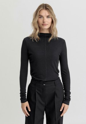 Haut noir à manches longues avec un col montant et une texture côtelée, associé à un pantalon noir ajusté avec une fermeture à bouton et des plis.