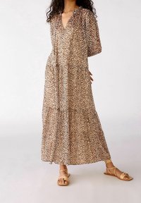 Abito maxi con stampa leopardata in tessuto trasparente, caratterizzato da una profonda scollatura a V, maniche a sbuffo e design a strati. Indossato con sandali piatti con cinturini.