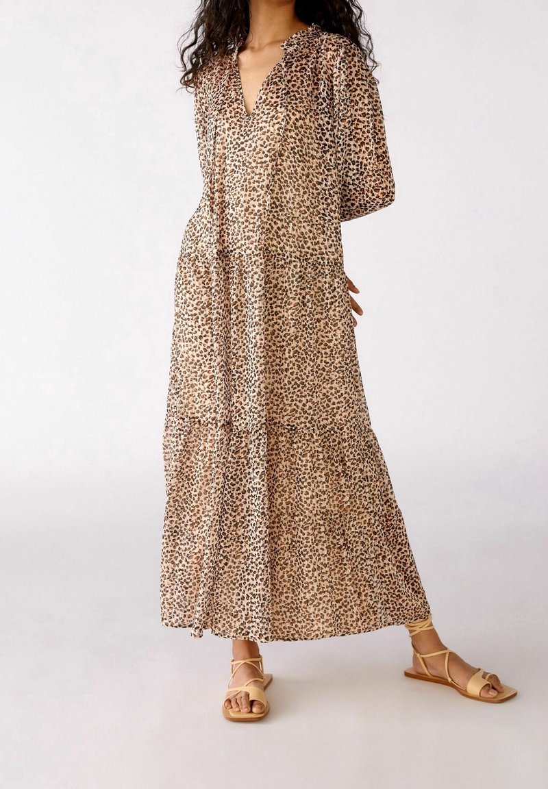 Abito maxi con stampa leopardata in tessuto trasparente, caratterizzato da una profonda scollatura a V, maniche a sbuffo e design a strati. Indossato con sandali piatti con cinturini.