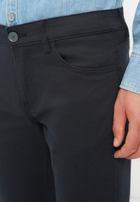 Sorte bukser laget av glatt stoff, med en frontlomme, beltehemper og knappelukking i midjen. Design med avslappet passform.