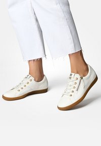 Weiße Ledersneaker mit goldenen Ösen, Schnürsenkeln und seitlichem Reißverschluss. Gummisohle mit braunen Akzenten. Flaches Design, strukturiert Oberfläche.