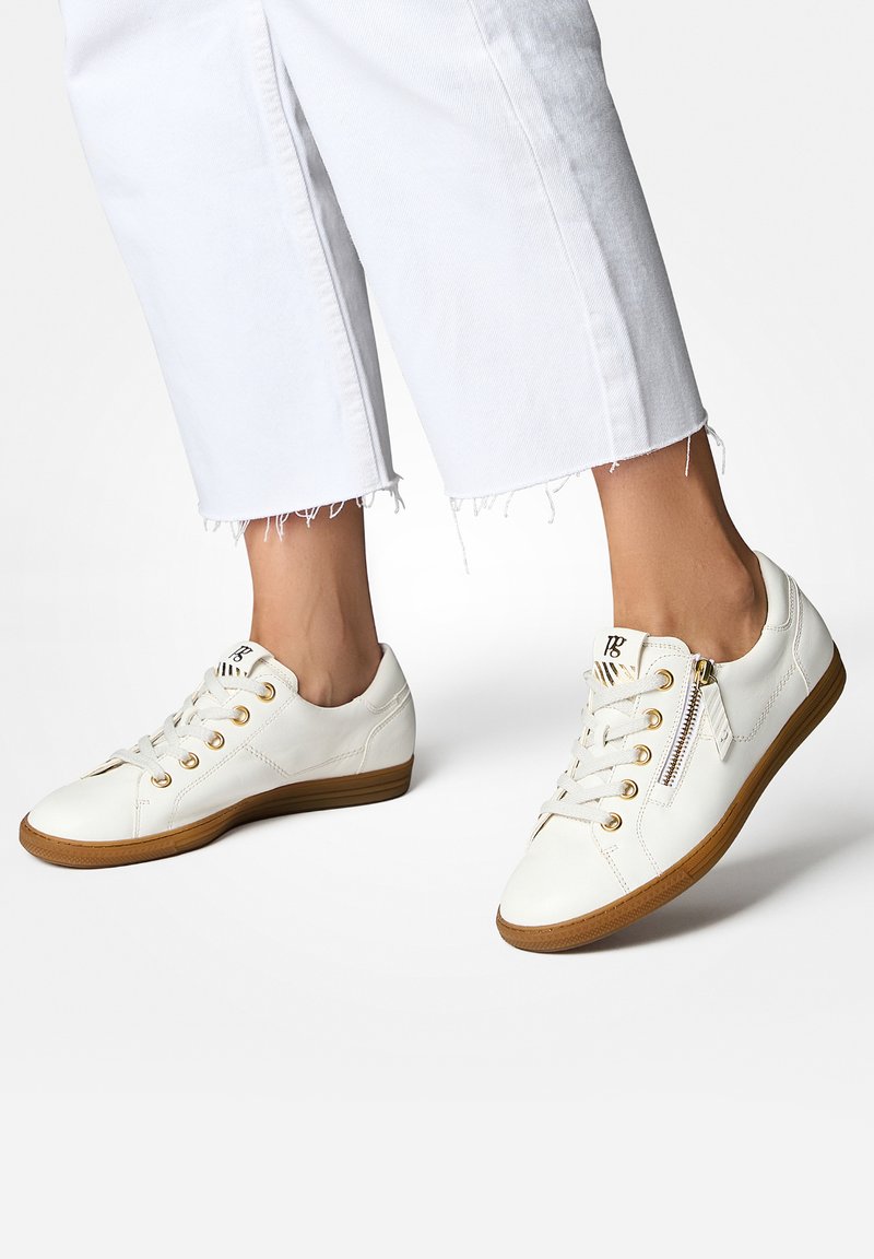 Weiße Ledersneaker mit goldenen Ösen, Schnürsenkeln und seitlichem Reißverschluss. Gummisohle mit braunen Akzenten. Flaches Design, strukturiert Oberfläche.