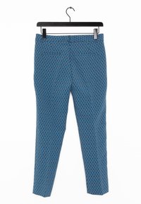 Blauwe broek met een geometrisch patroon. Tailored fit, platte voorkant, zijzakken en een gladde textuur. Hangt aan een zwarte haak.