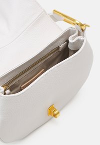 Sac à main en cuir blanc texturé avec ouverture supérieure, intérieur beige, poche zippée dorée et fermeture à tourniquet dorée sur fond blanc.
