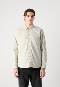Light beige button-up shirt with two chest pockets, long sleeves, and a point collar, made from a smooth, lightweight fabric.